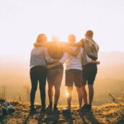 A group of friends standing on top of a mountain at sunset.