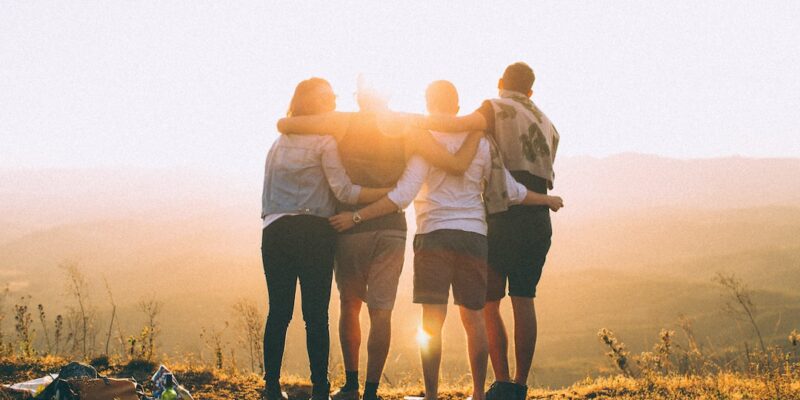 A group of friends standing on top of a mountain at sunset.