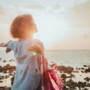 A woman standing on the beach with her arms outstretched.