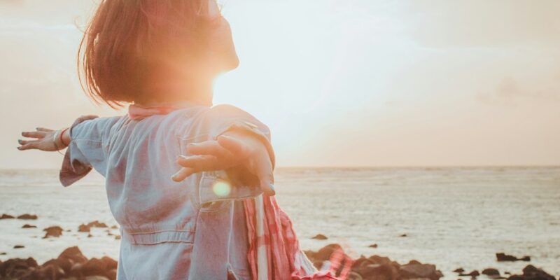 A woman standing on the beach with her arms outstretched.