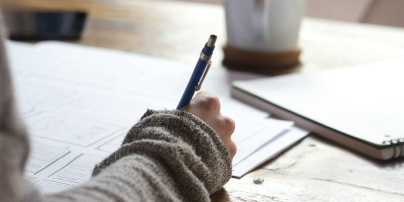 A person writing on a piece of paper at a desk.