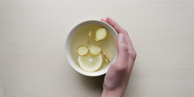 A person holding a bowl of lemon tea on a wooden table.