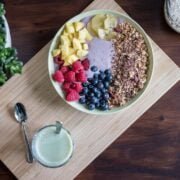 A bowl of fruit and granola on a wooden cutting board.