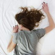 A woman laying on a white bed with her head down.