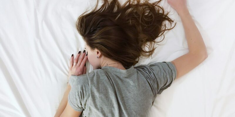 A woman laying on a white bed with her head down.