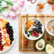 A bowl of fruit, a bowl of oatmeal and a cup of coffee on a wooden cutting board.