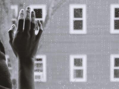 A black and white photo of a hand reaching out of a window.