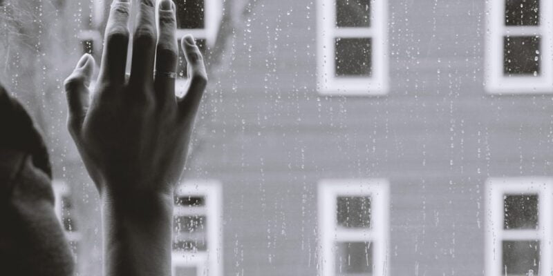 A black and white photo of a hand reaching out of a window.