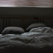 A bed in a dark room with blinds.