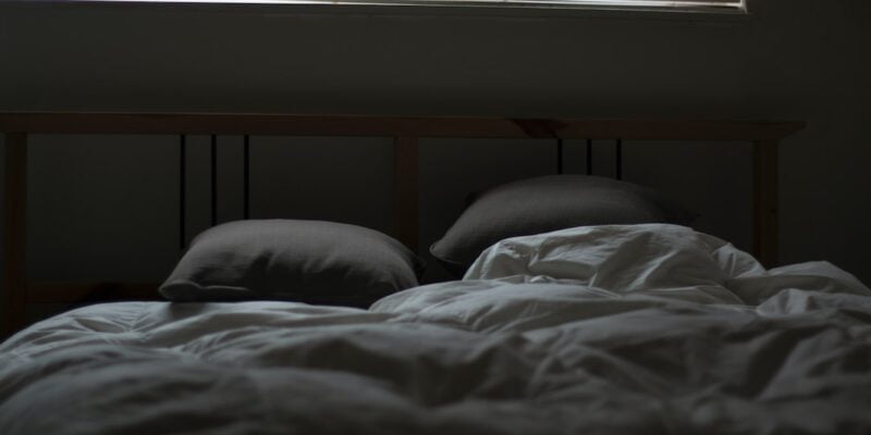 A bed in a dark room with blinds.