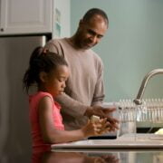 An african-american man and his daughter washing dishes in the kitchen.