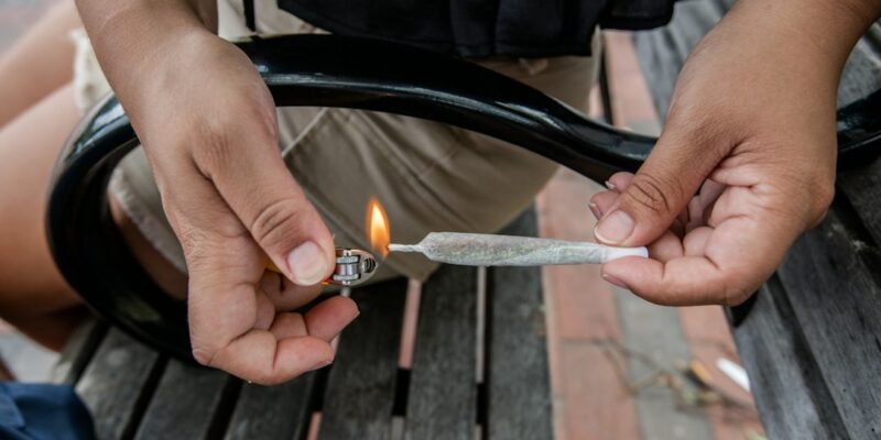 A person holding a lighter while sitting on a bench.