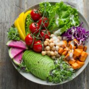 A bowl full of vegetables and fruits on a wooden table.