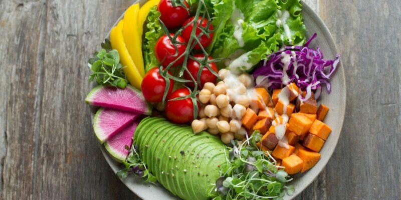 A bowl full of vegetables and fruits on a wooden table.