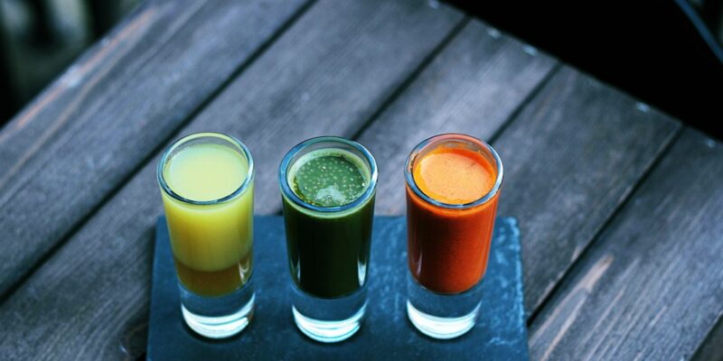 Three glasses of juice sitting on a wooden table.