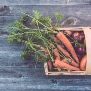 A wicker basket full of vegetables on a wooden table.