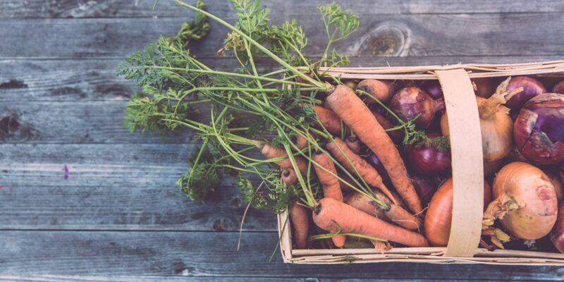 A wicker basket full of vegetables on a wooden table.