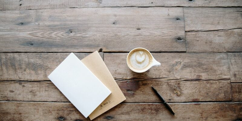 A cup of coffee and a notebook on a wooden table.