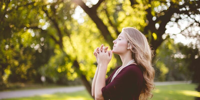 A young woman praying in a park.