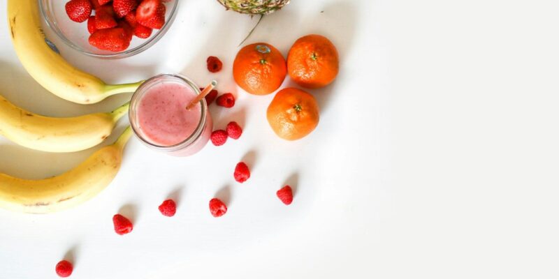 A group of fruits and a smoothie on a white table.