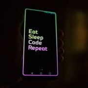 A person holding a phone that says eat sleep code repeat.