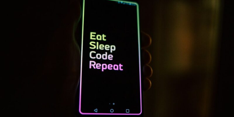 A person holding a phone that says eat sleep code repeat.