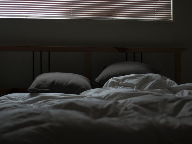 A bed in a dark room with blinds.