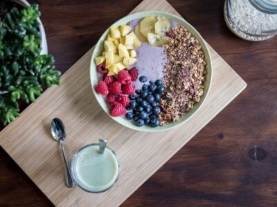 A bowl of fruit and granola on a wooden cutting board.