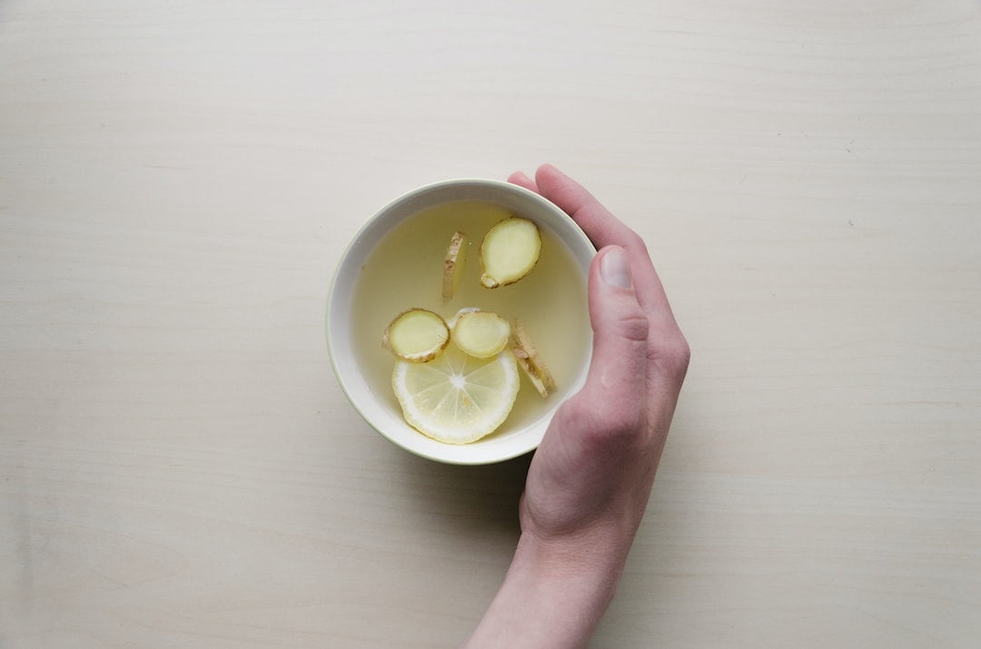 A hand holding a bowl of water with lemon slices.