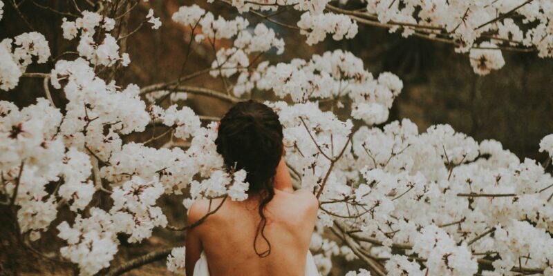 A woman standing under a tree with white flowers.