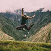 A woman jumping in the air on top of a mountain.