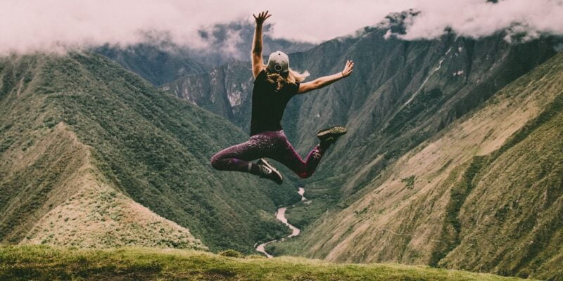 A woman jumping in the air on top of a mountain.