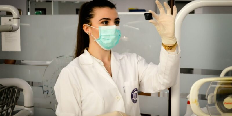 A woman wearing a lab coat and gloves in a dental office.