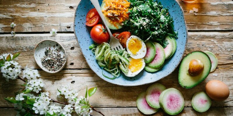 A bowl of salad with eggs and vegetables on a wooden table.