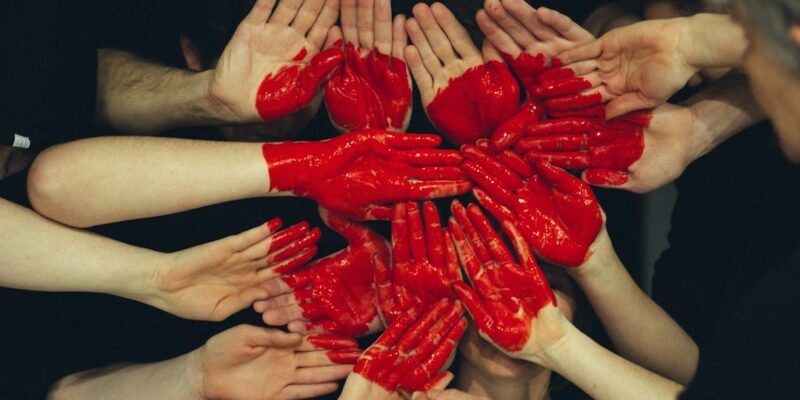 A group of people with red painted hands in a circle.