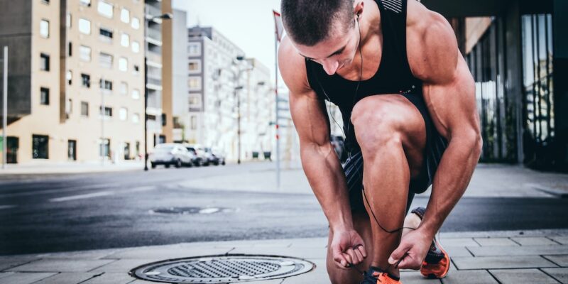 A man tying his shoes on the sidewalk.