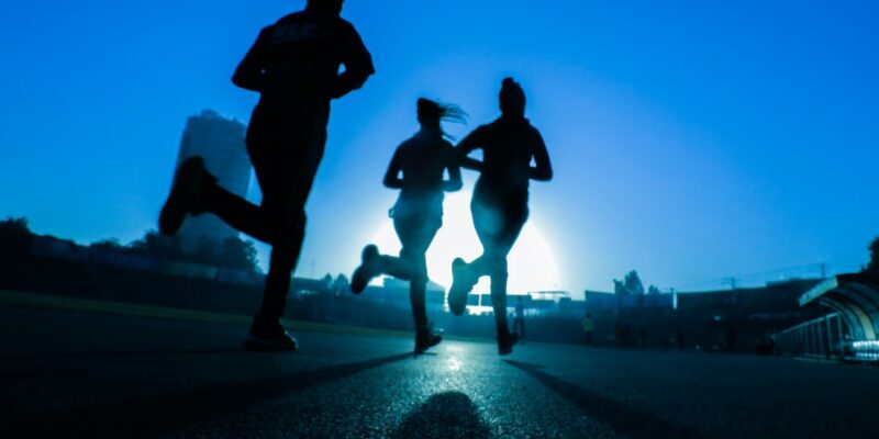 Silhouettes of people running on a road at sunset.