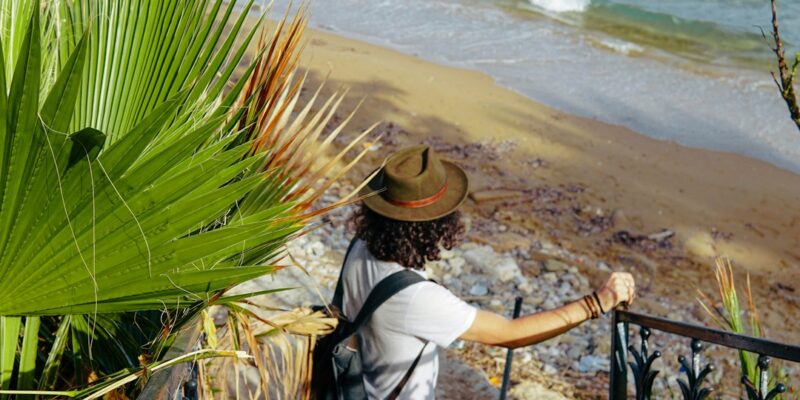 A man wearing a hat is standing on a railing near a beach.