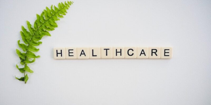 The word healthcare is written in scrabble letters on a white background with a fern leaf.