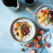 Two bowls of oatmeal with fruit and berries on a blue table.