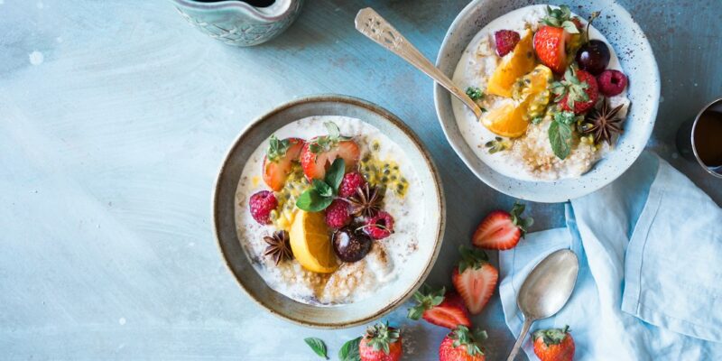 Two bowls of oatmeal with fruit and berries on a blue table.