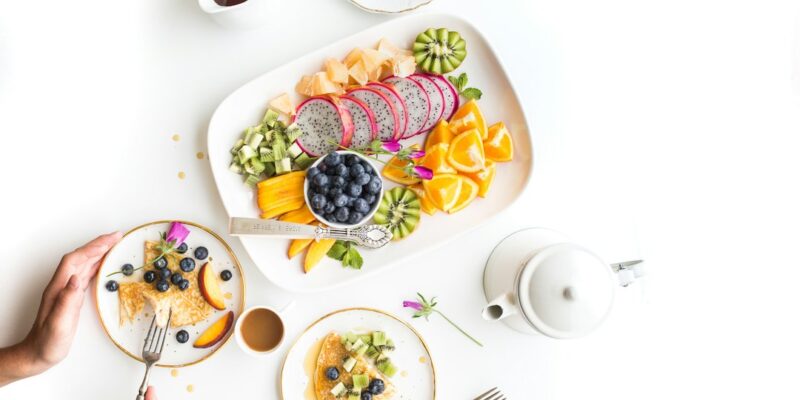 A woman is holding a plate of fruit and a cup of coffee.