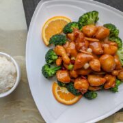 A plate of orange chicken with rice and broccoli.