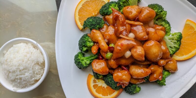 A plate of orange chicken with rice and broccoli.