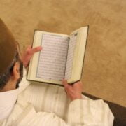 A man in a hat is reading the quran.