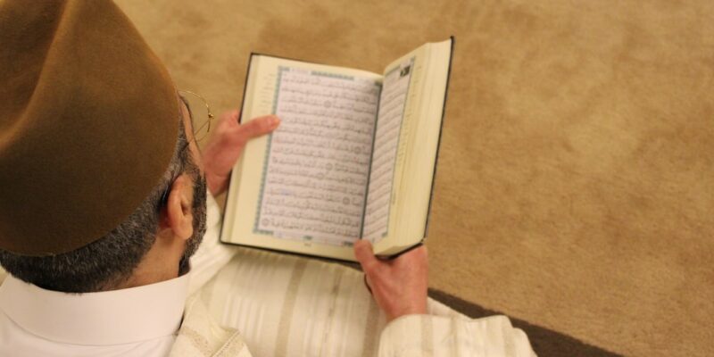 A man in a hat is reading the quran.