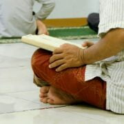 A man sitting on the floor reading a book.