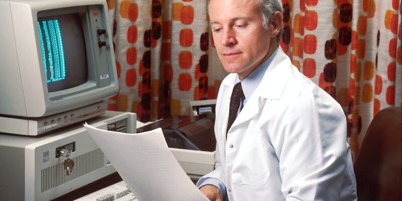 A man in a white lab coat reading a paper.