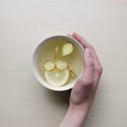 A hand holding a bowl of water with lemon slices.