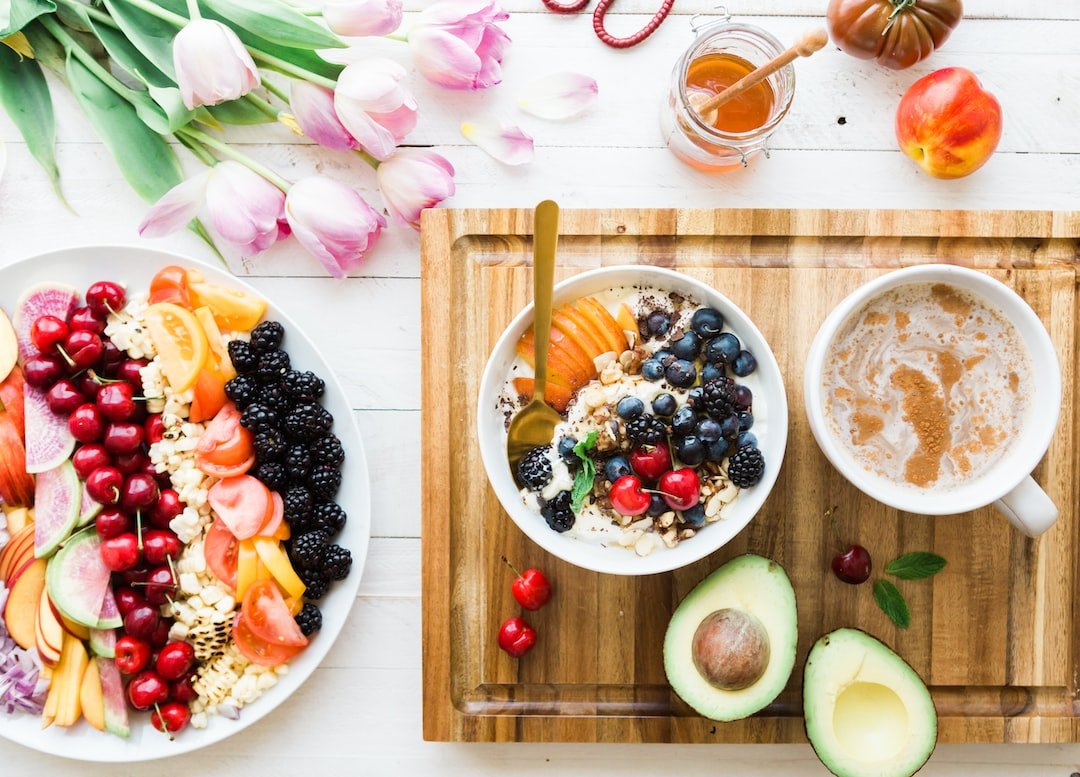 A bowl of fruit and a bowl of coffee on a wooden tray.